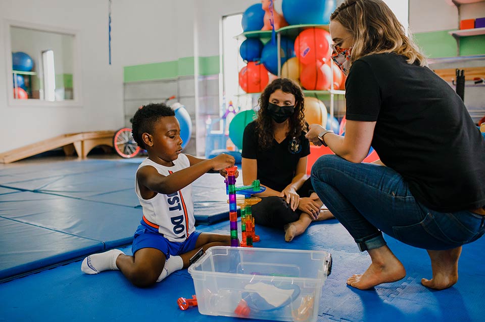 Photo of two therapists and a little boy playing with a toy