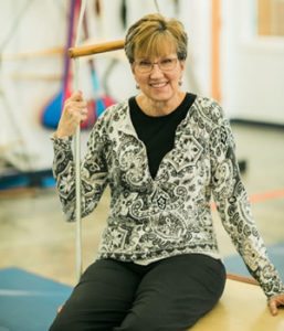 Therapy aide Deb Van Deman seated on a platform swing in the sensory gym