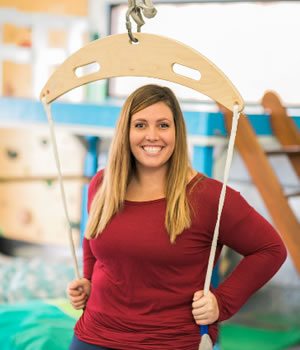 Occupational Therapist Jaclyn Jewett wearing red while seated on a frog swing