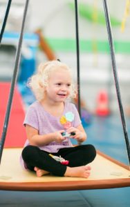 young girl sitting on a platform swing in the sensory gym for speech therapy