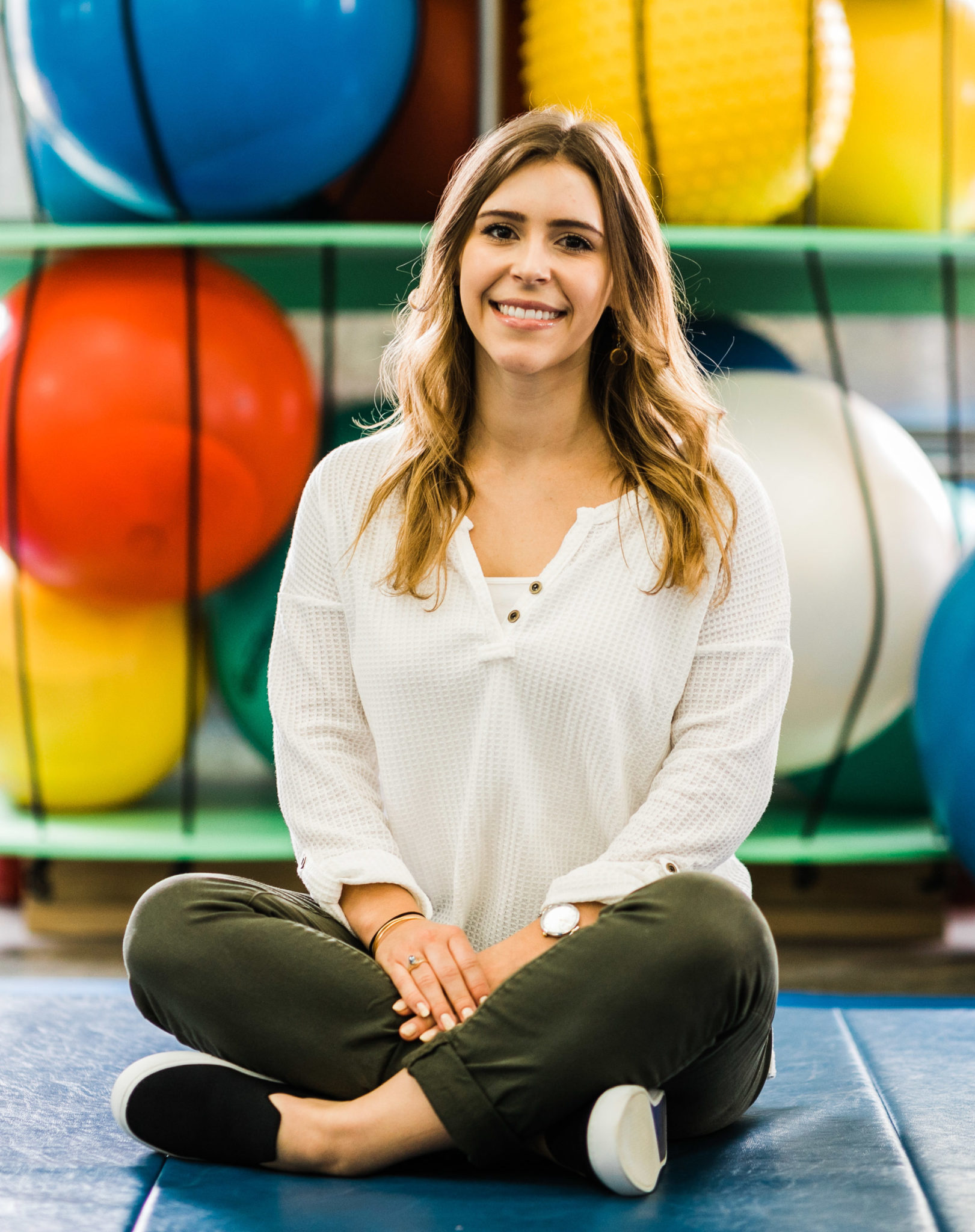 Rachel Keen, therapy aide, wearing a white top with olive pants sitting in the sensory gym