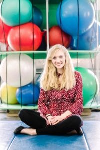 Speech Language Pathologist Taylor Taylor, wearing a red top with black pants, sitting in a sensory gym