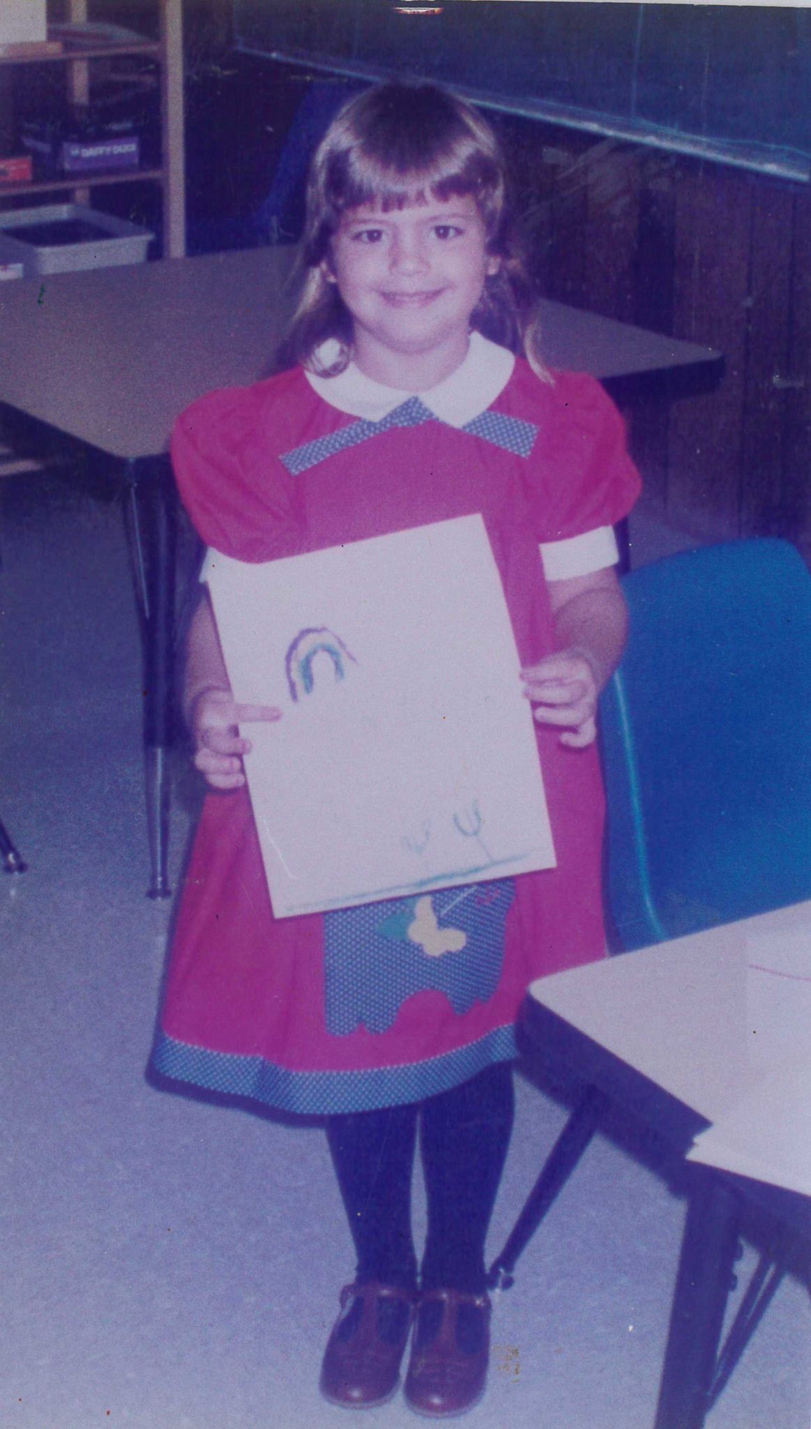 Occupational Therapist Nicole as a young girl, wearing a red dress showing her picture in a classroom