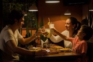 family of three toasting their glasses while eating at a pizza restaurant