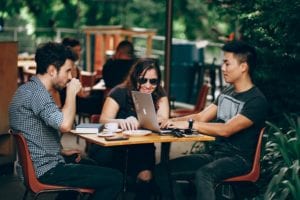 three young adults made up of two males and one female, drinking coffee and working on a group project