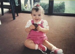 Occupational Therapist Jakelyn as a toddler, wearing pink overalls with a large cookie in her hands