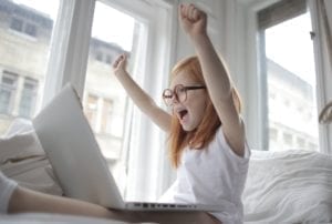young girl excited and cheering with her hands up while using a laptop computer
