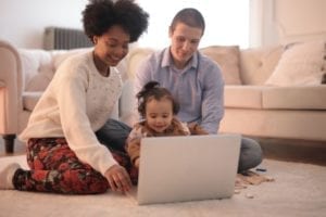 young family of three, sitting on the floor while using a laptop