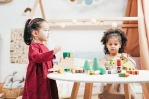 two young girls playing with dinosaur wooden toys at a table