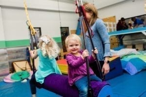 two girls swinging in a sensory gym as an occupational therapist stands by