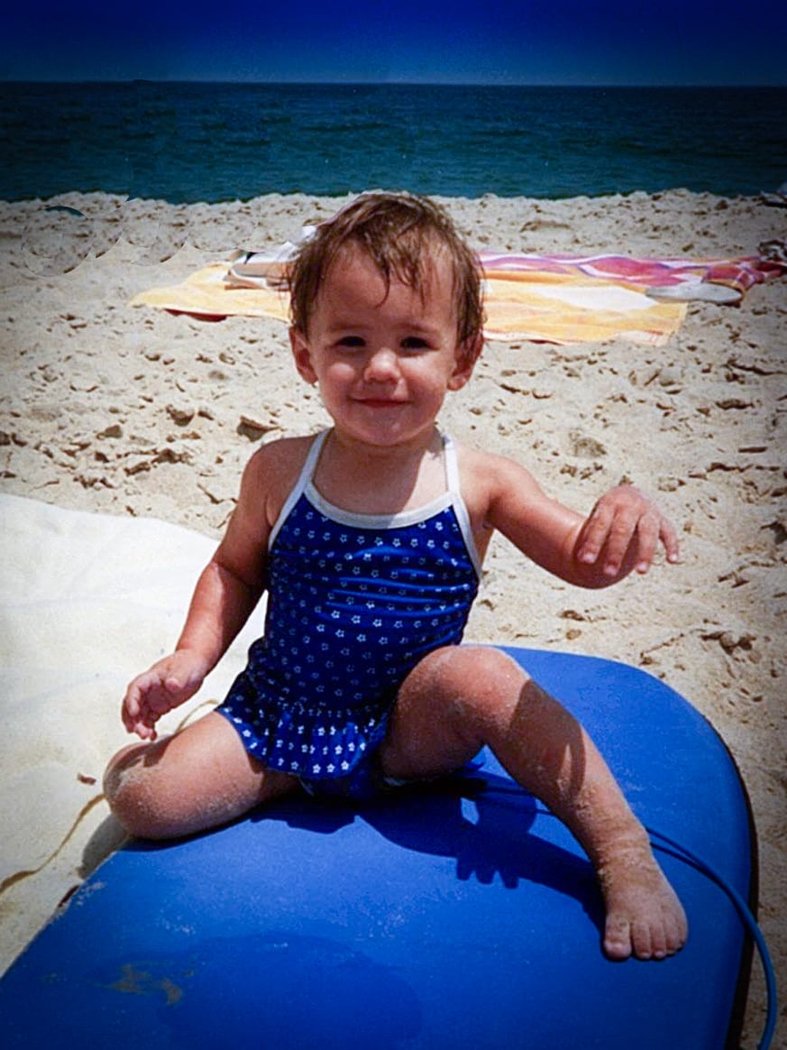 Speech Language Pathologist Danielle as an infant wearing a blue swimsuit sitting on a blue float at the beach