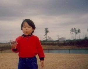 Occupational Therapist Taz as a young boy wearing red shirt and blue jeans eating a pie while walking close to a lake with dark clouds above