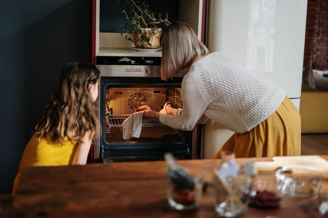 young girl and mother take a dish out of the oven