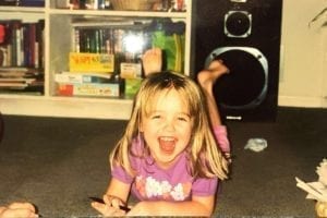 Community Engagement Coordinator Molly as a young girl lying on her stomach while smiling at the camera