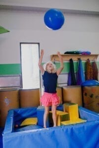 Young girl playing catch with a blue therapy ball while standing in a foam pit