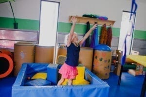 Young girl playing catch with a blue therapy ball while standing in a foam pit