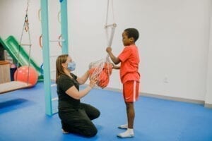 Boy and Occupational Therapist putting Elmo into a net swing