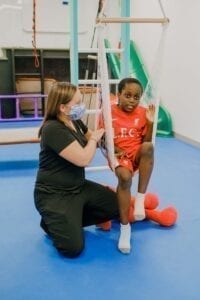 Boy sitting in a net swing while an occupational therapist pushes the swing