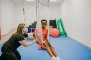 Boy sitting in a net swing while an occupational therapist pushes the swing