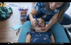 Speech therapist leans over a small child with her mouth open. Speech therapist is using a z vibe inside the child's mouth.