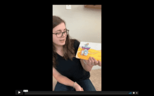 Brunette therapist in glasses looks at an open book she is holding upright