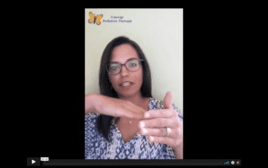 brunette, female therapist in glasses, holding her hands up near her face to demonstrate an oral resting posture