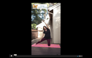 white, female, therapist in dark colored yoga clothes stretches her arm over her head and her leg out to the side on a pink yoga mat.