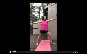 White, female, therapist in black gym short and bright pink top does warrior 2 yoga pose on a pink yoga mat