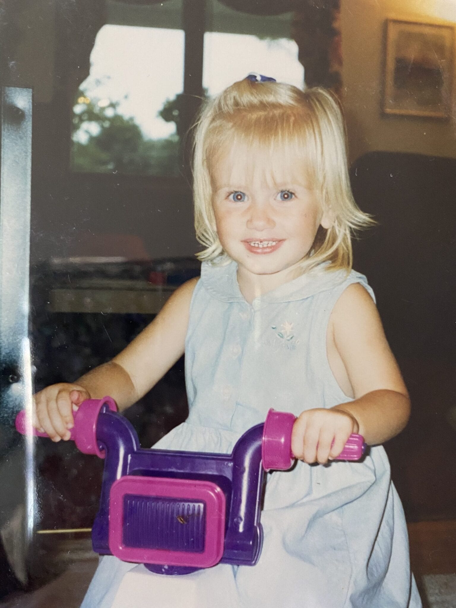 toddler girls in a blue dress rides a purple bike